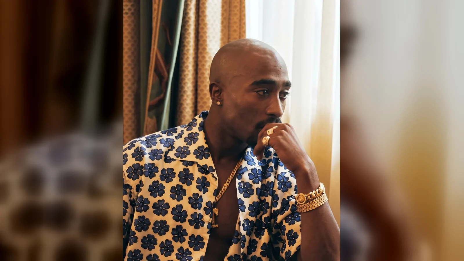 Tupac Shakur assis près d’une fenêtre, vêtu d’une chemise à fleurs bleues, photographié par Ken Nahoum.