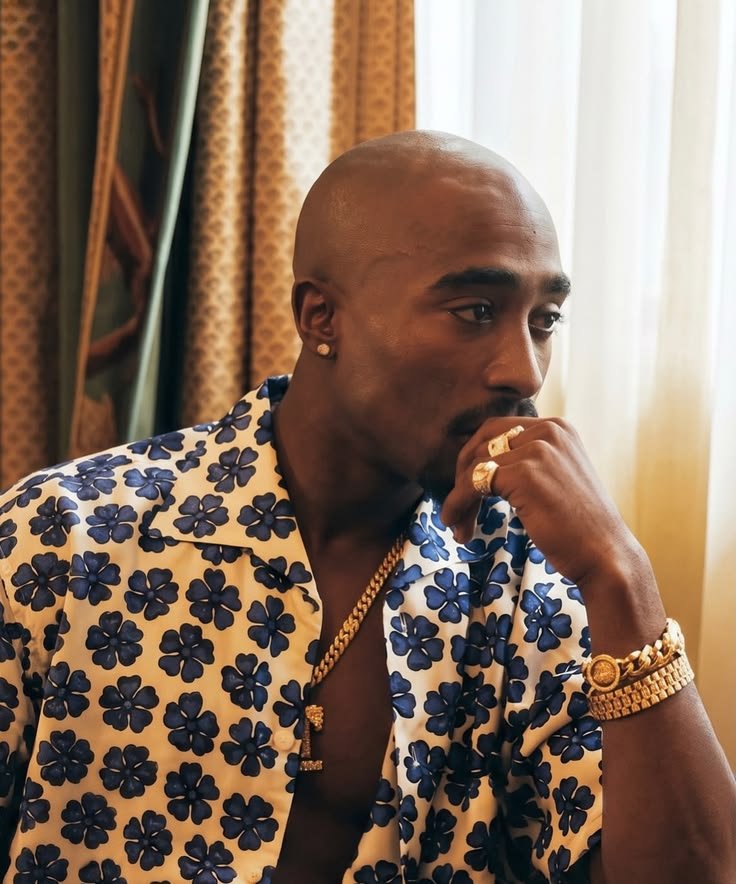 Tupac Shakur assis près d’une fenêtre, vêtu d’une chemise à fleurs bleues, photographié par Ken Nahoum.