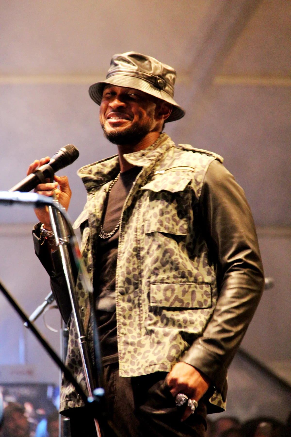 Usher sourit au micro, en bob de cuir et veste à motif léopard, sur une petite scène.