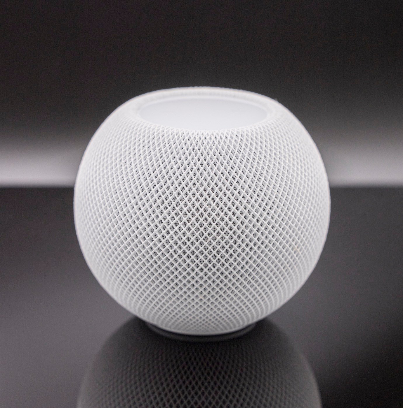 Un HomePod mini blanc posé sur une surface sombre.