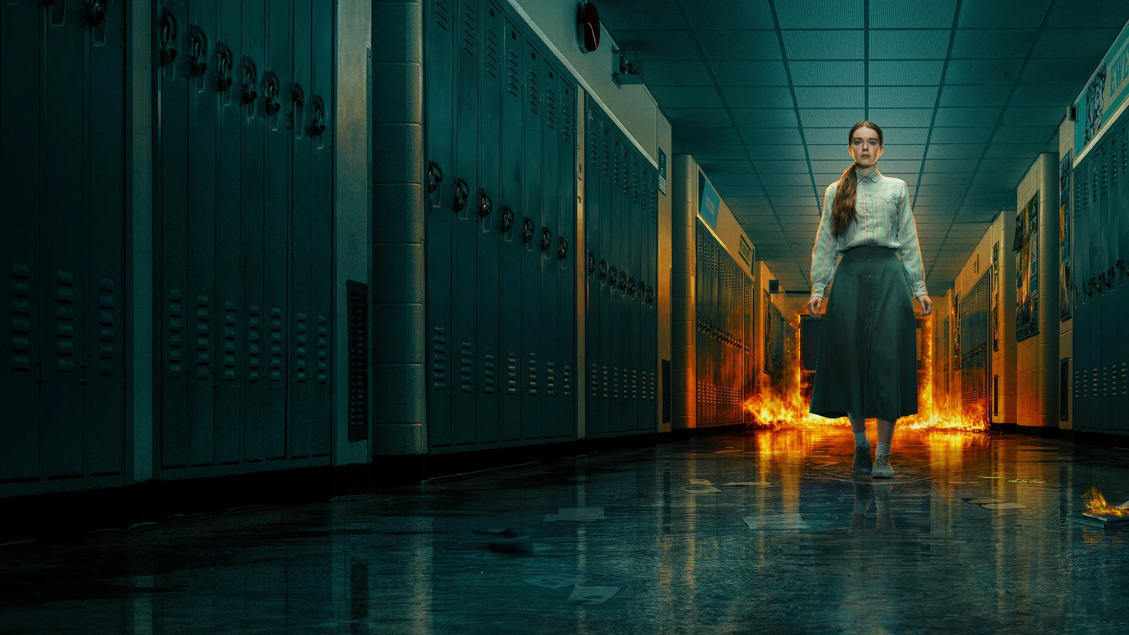 Une adolescente aux cheveux longs, en chemisier clair et jupe longue, avance seule dans un couloir de lycée bordé de casiers, tandis que des flammes s’élèvent derrière elle.