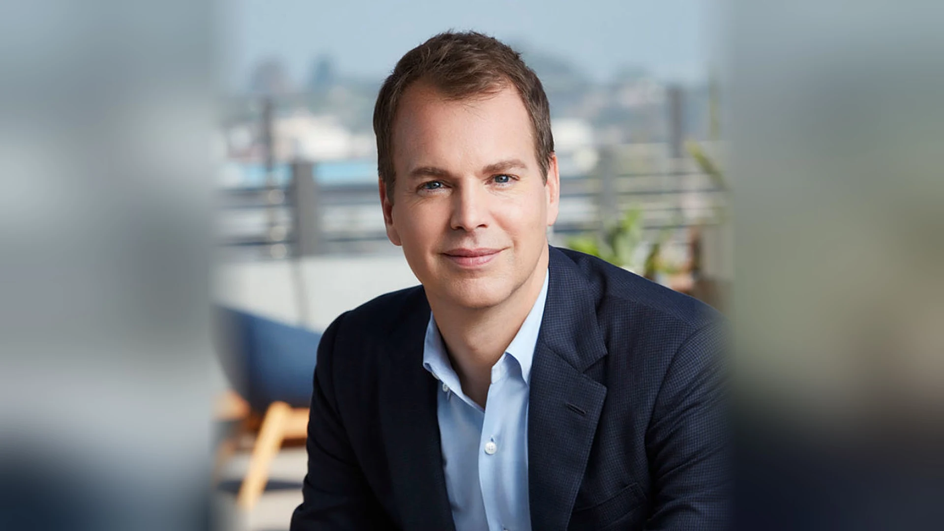 Portrait de Casey Bloys, président de HBO et des contenus de HBO Max : un homme souriant, en veste bleu marine et chemise bleu ciel, sur une terrasse.
