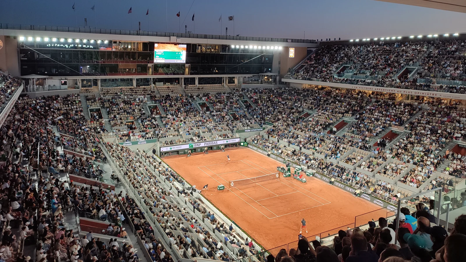 Le court Philippe-Chatrier de Roland-Garros plein, éclairé à la tombée de la nuit, pendant une session du soir en 2023 : la terre battue au centre, les tribunes garnies tout autour.