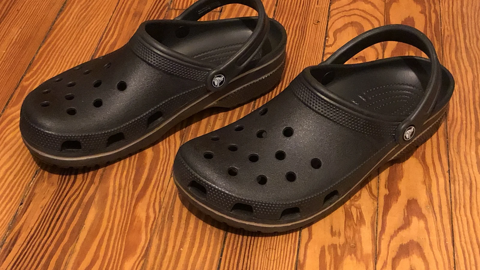 Une paire de sabots Crocs Classic noirs posée sur un parquet en bois.