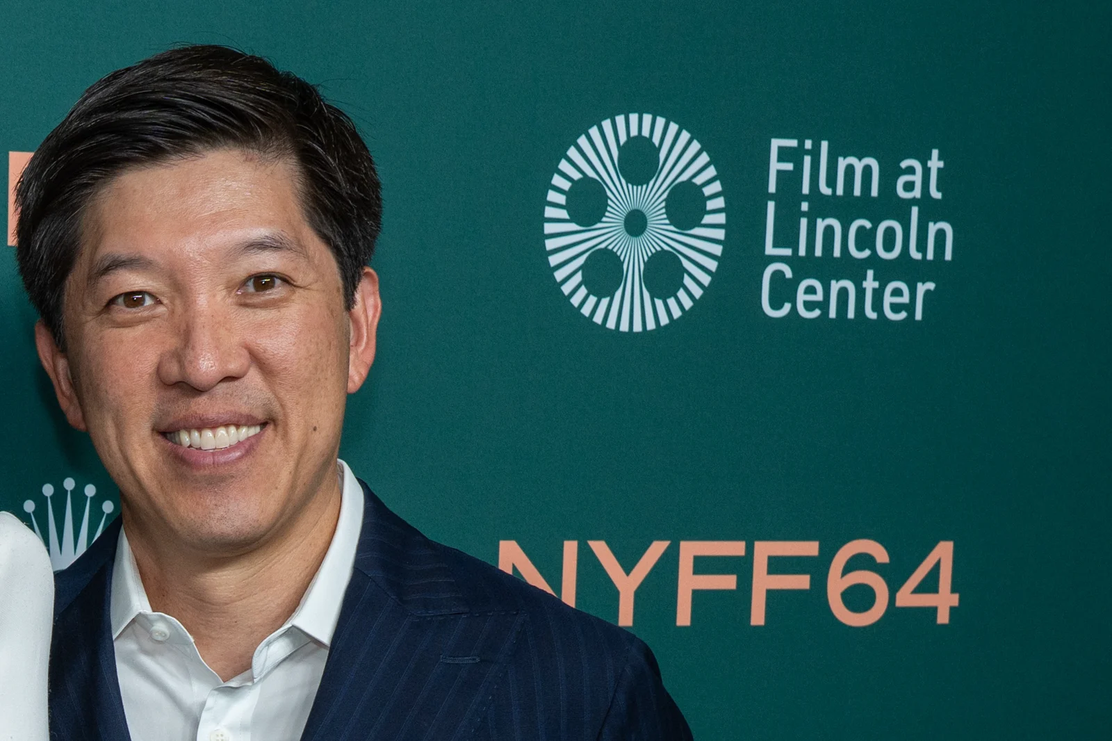 Dan Lin, souriant, en costume bleu marine à fines rayures et chemise blanche, devant le panneau vert du New York Film Festival.
