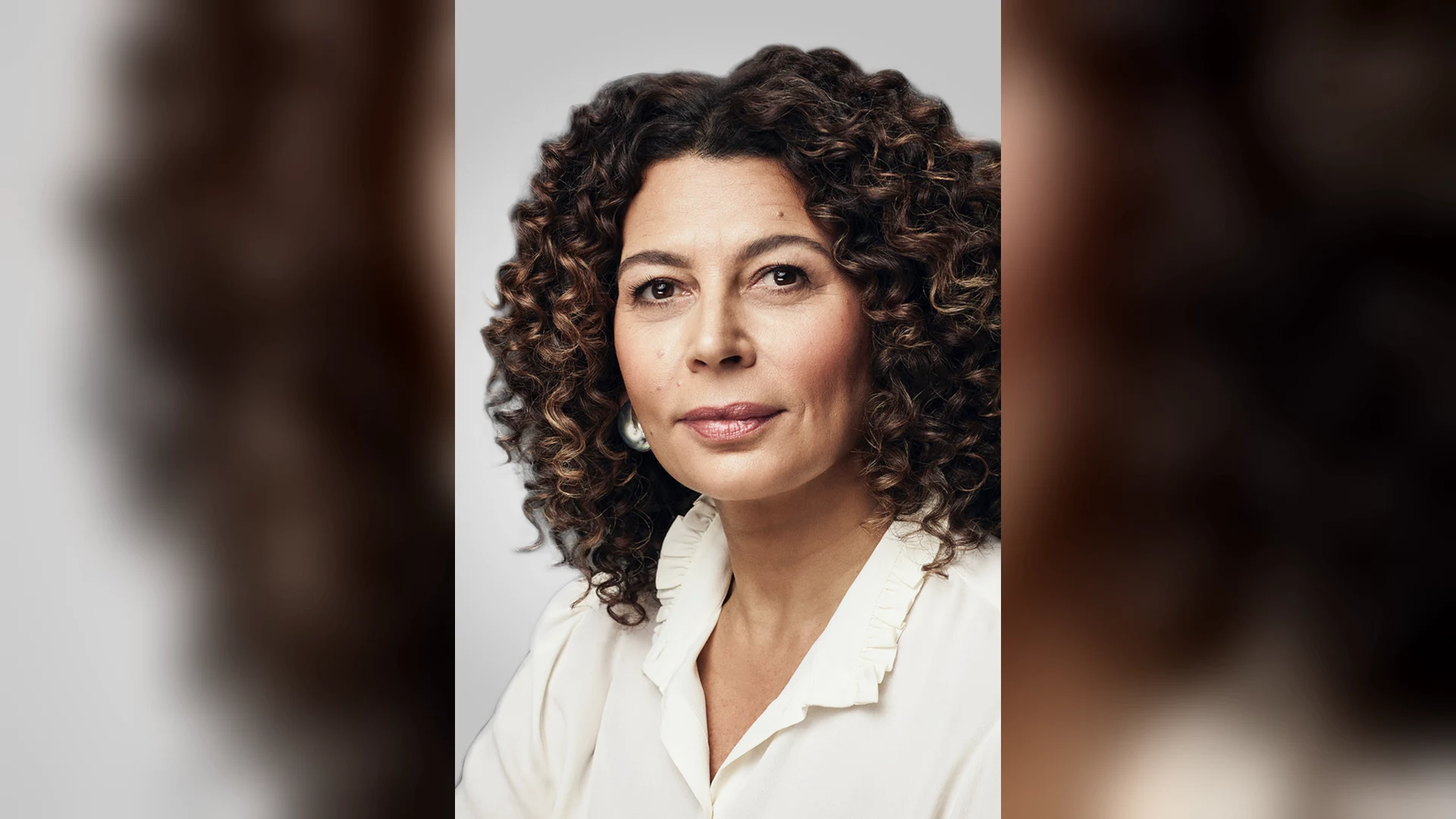 Portrait de Donna Langley, présidente de NBCUniversal Entertainment : une femme aux cheveux bouclés, en chemisier blanc à col volanté, sur fond gris clair.