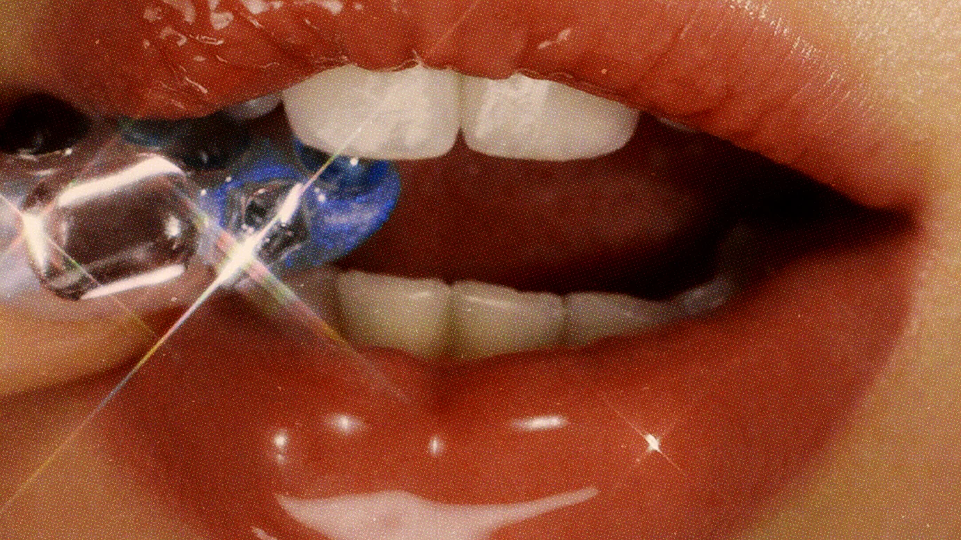 Gros plan sur des lèvres rouges brillantes tenant un bijou de dent en cristal, visuel de l’album « Mirror Mix » d’e.l.f.