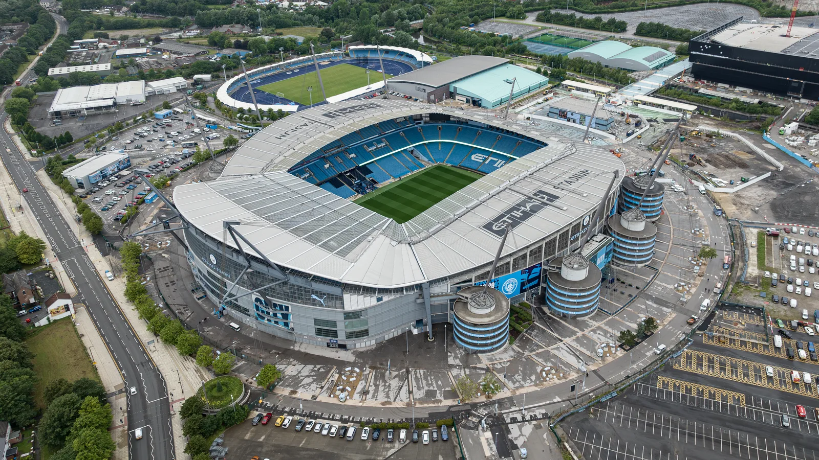 Vue aérienne de l’Etihad Stadium de Manchester City, son toit blanc et sa pelouse, entouré de parkings et de l’Etihad Campus.