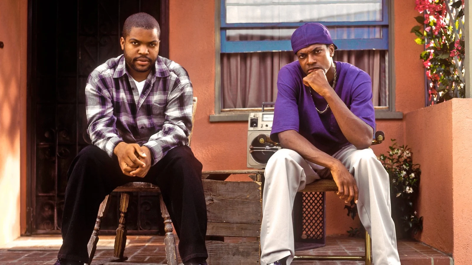 Ice Cube, chemise à carreaux violette, et Chris Tucker, tee-shirt violet et casquette, assis sur deux chaises devant une maison rose, un poste de radio entre eux.