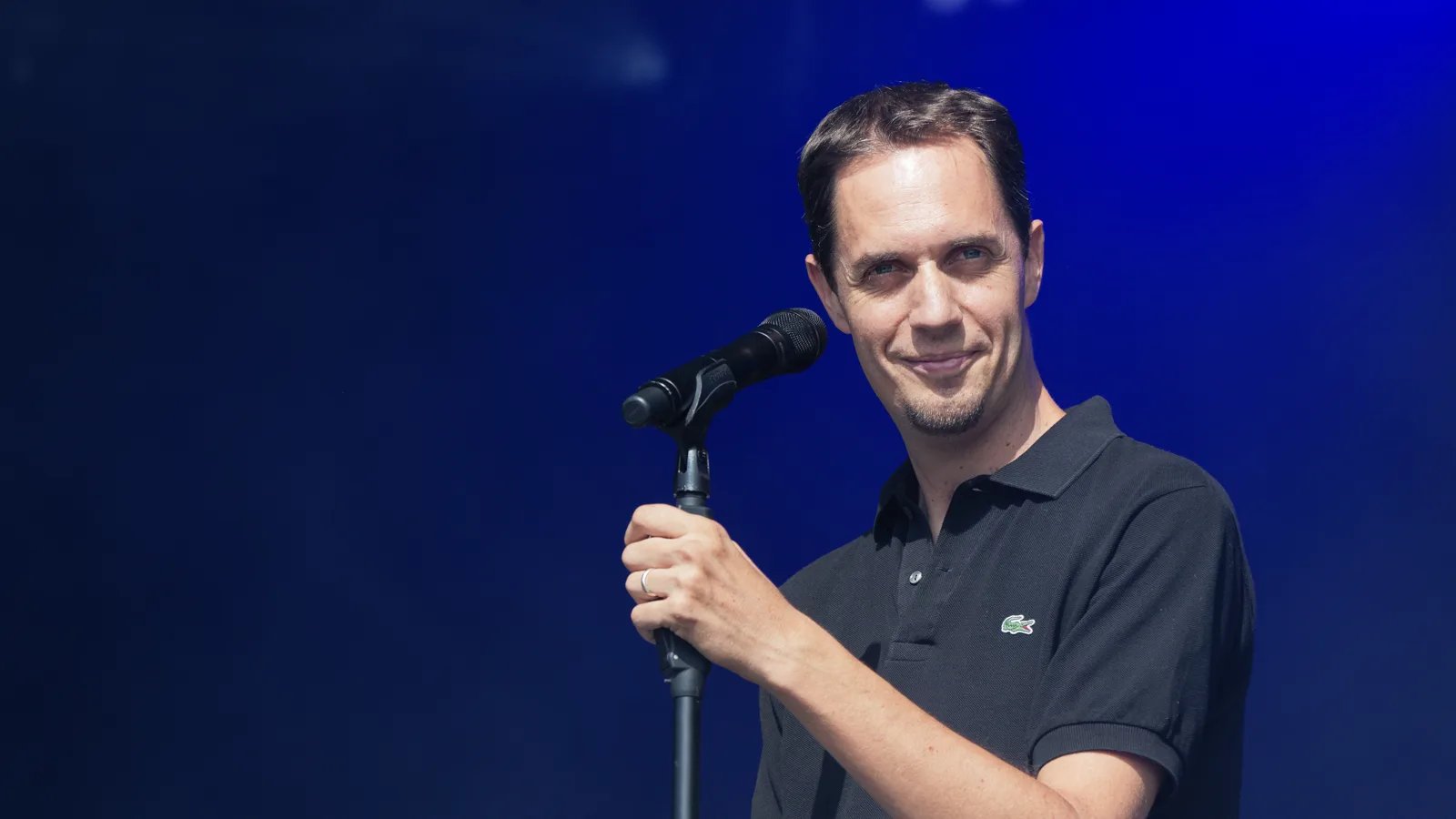Grand Corps Malade au micro sur scène, devant un fond bleu, au Festival du Bout du Monde en 2018.