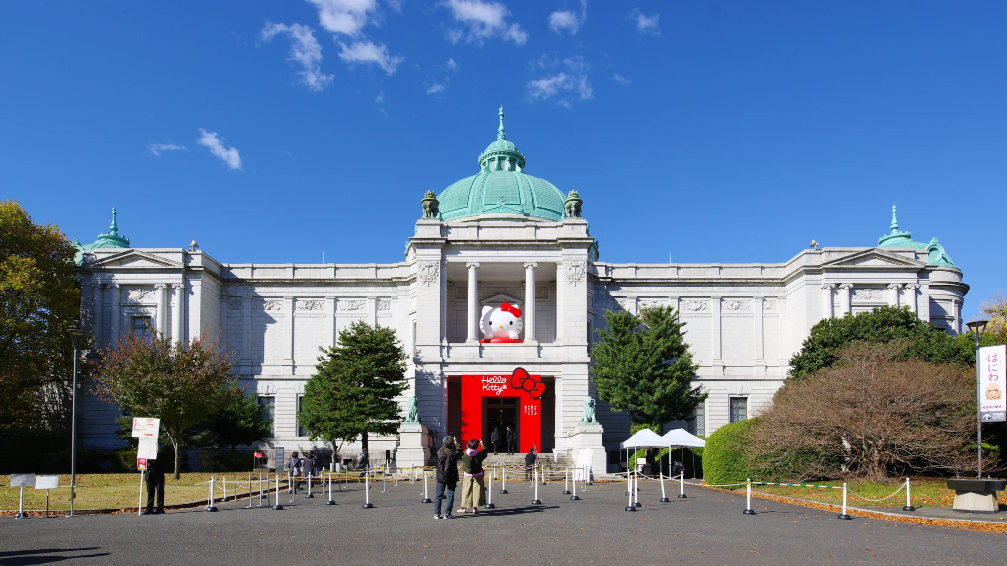 La façade blanche à coupole verte du Hyōkeikan, au Musée national de Tokyo, avec une grande tête de Hello Kitty au-dessus de l’entrée habillée de rouge, sous un ciel bleu.