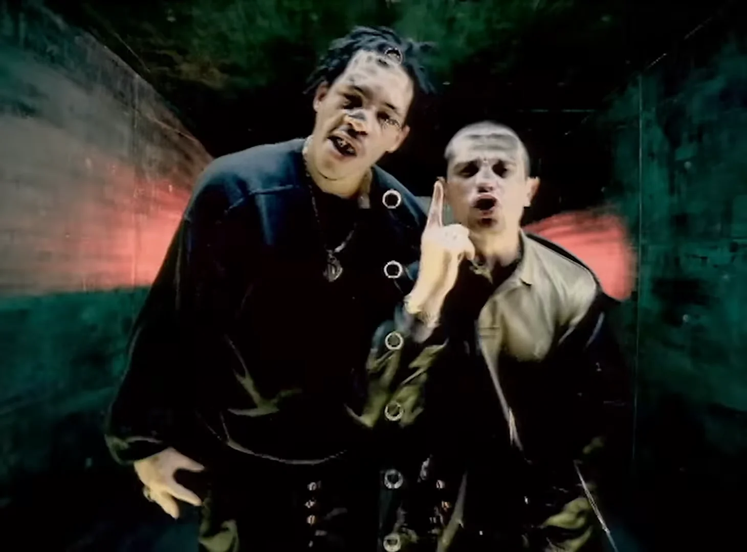 JoeyStarr et Kool Shen côte à côte, filmés au grand angle dans un décor sombre aux reflets verts et rouges ; l’un des deux lève l’index.
