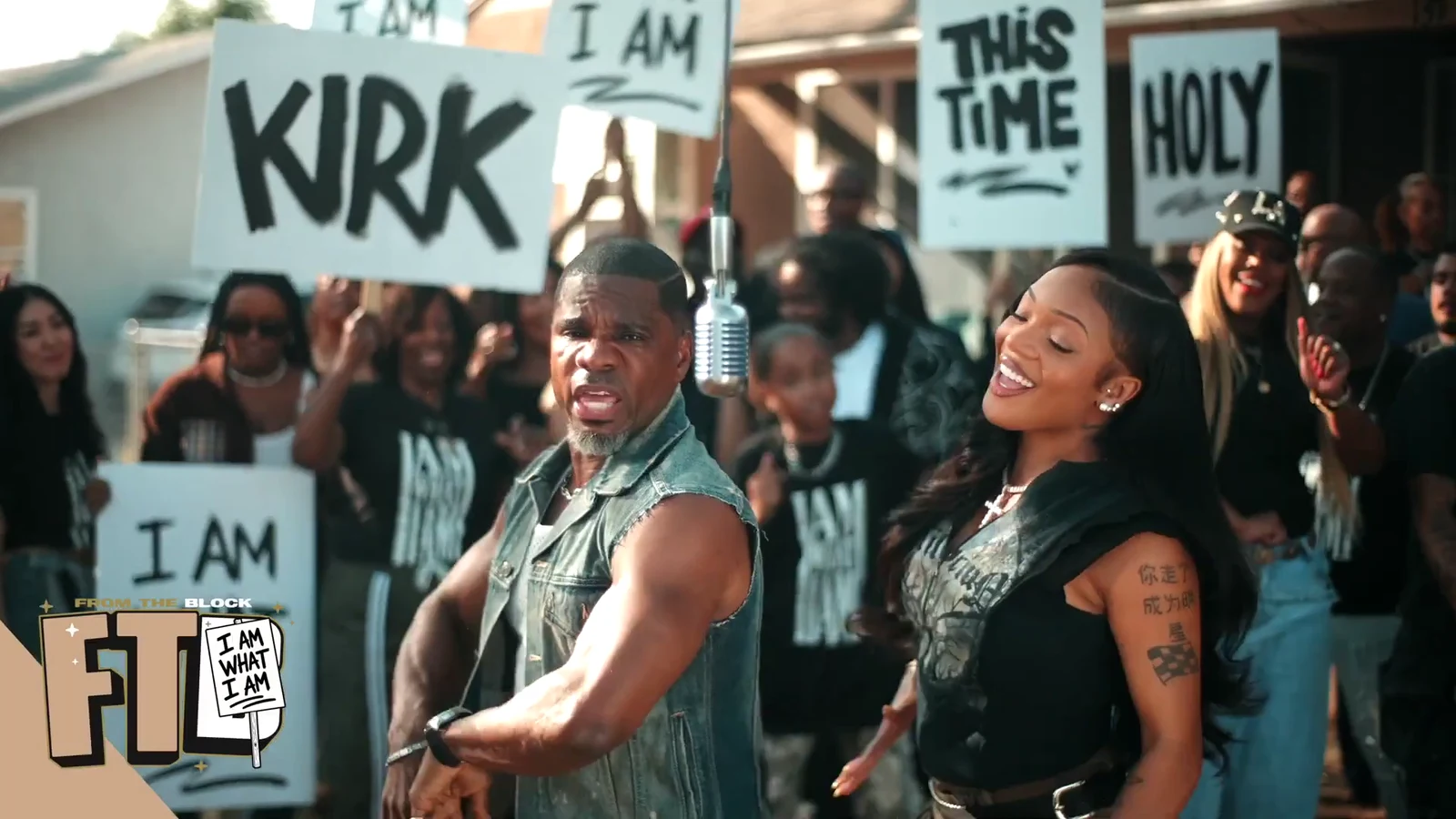 Kirk Franklin, en gilet en jean, et GloRilla, souriante, dansent devant une foule qui brandit des pancartes « KIRK », « THIS TIME », « HOLY » et « I AM ».