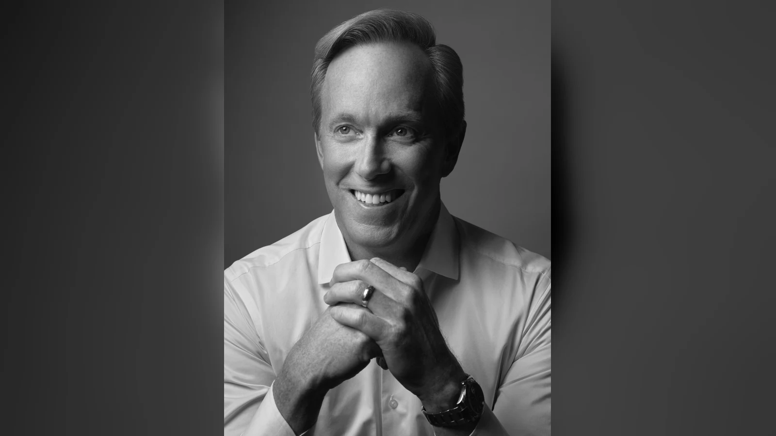 Portrait en noir et blanc de Roger Lynch, nommé président puis directeur général de Mattel : un homme souriant, en chemise blanche, les mains jointes devant le visage, le regard tourné vers la gauche.