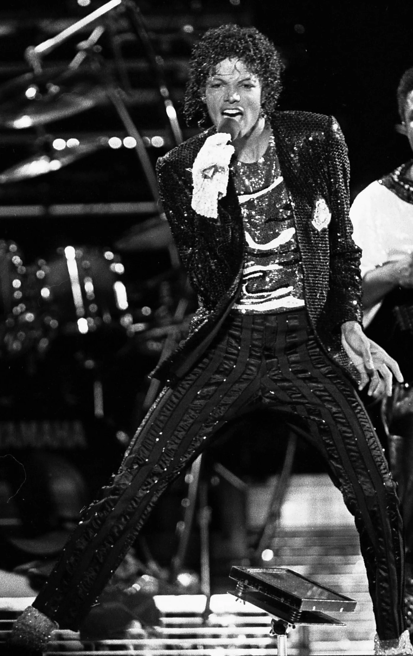 Michael Jackson chante sur scène en veste à paillettes et gant blanc, jambes écartées, pendant le Victory Tour en 1984.