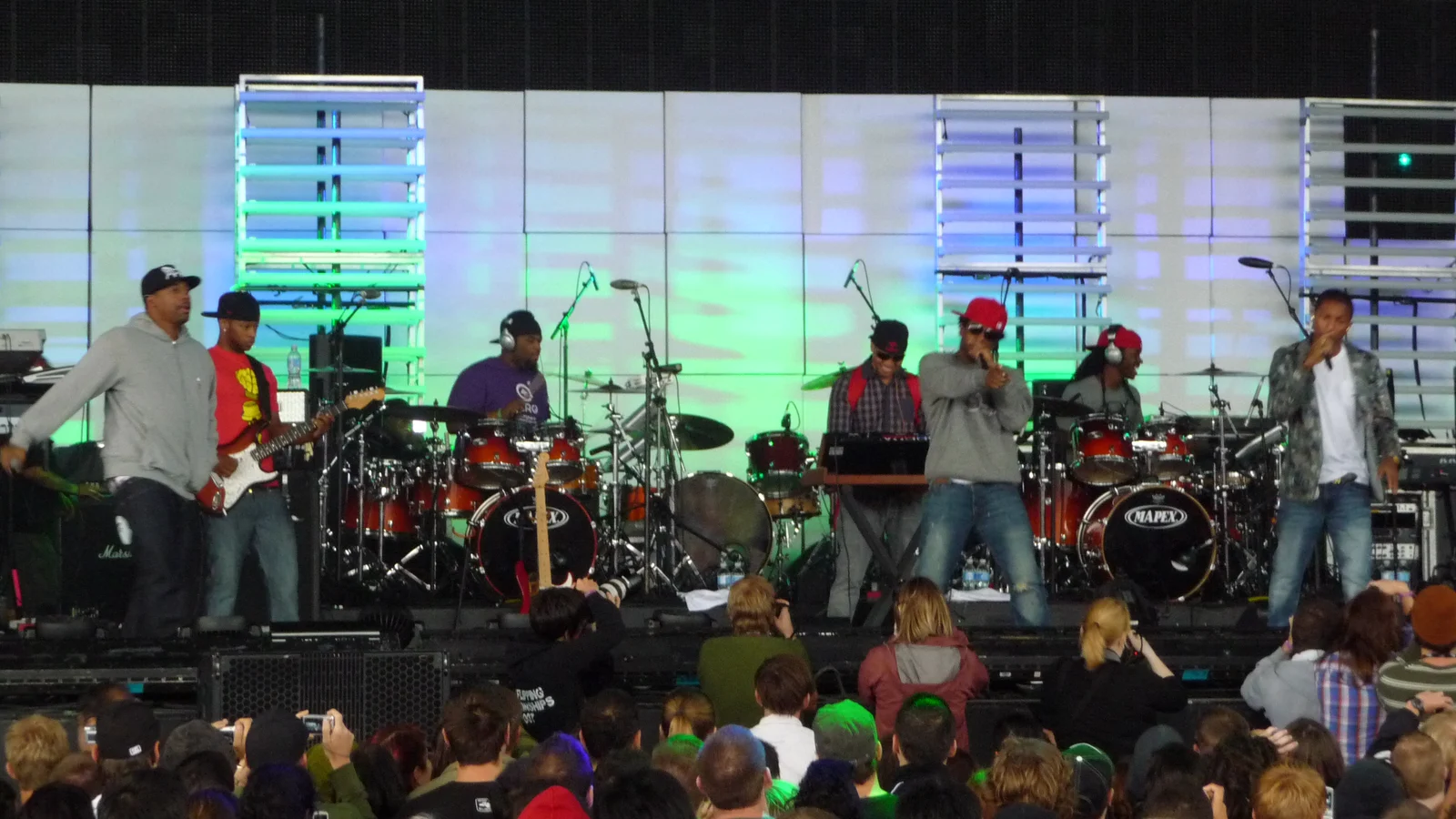 Le groupe N.E.R.D. sur la scène du Virgin Festival Ontario en août 2009 : deux chanteurs au micro, un claviériste, des batteurs et un guitariste devant un mur lumineux vert et bleu, le public de dos au premier plan.