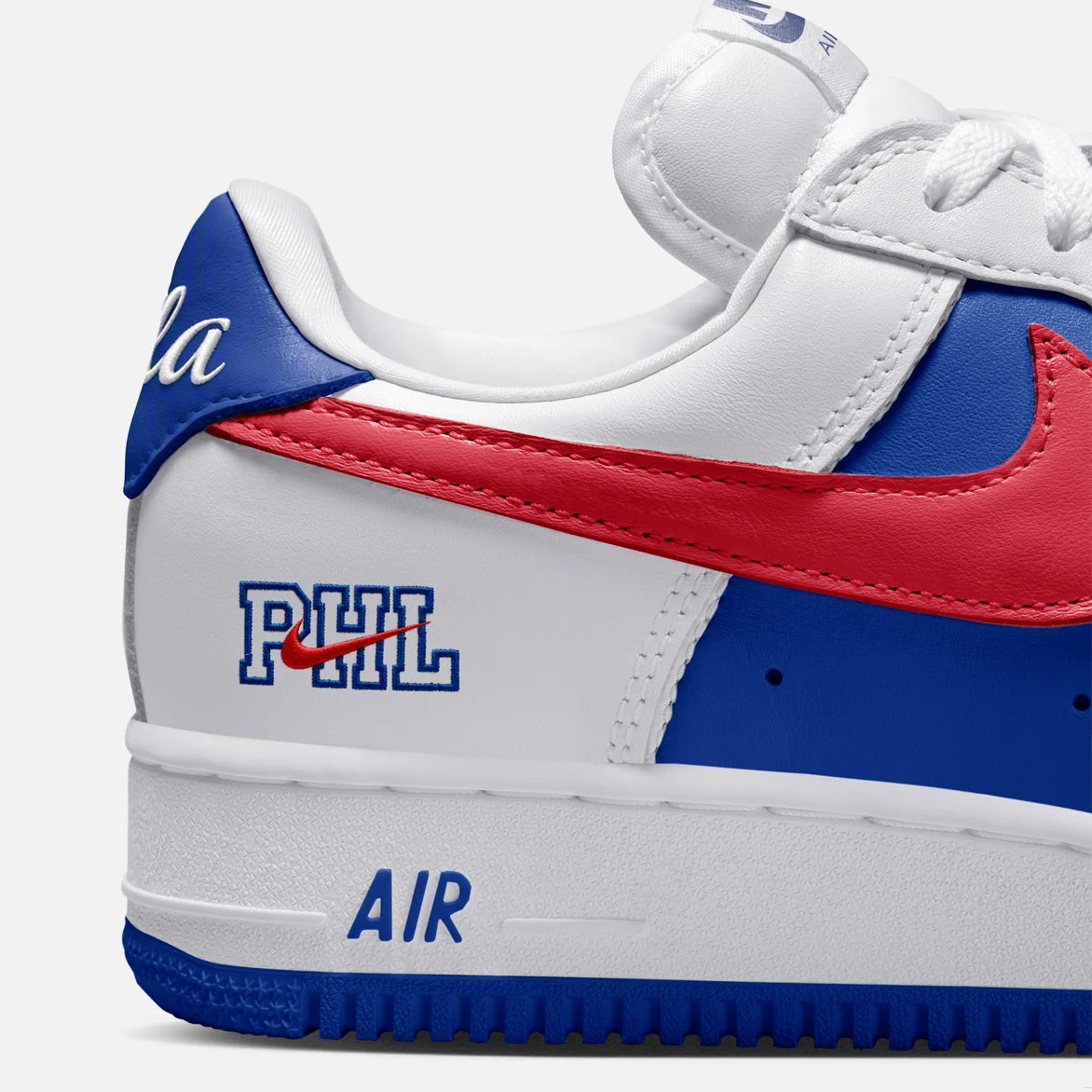 Gros plan sur le talon de l’Air Force 1 « Philly » : « PHL » brodé en bleu avec un mini Swoosh rouge, et le script « Phila » sur la languette arrière.