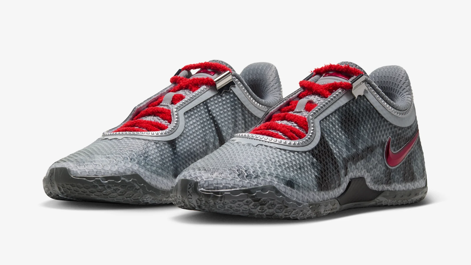 Une paire de Nike LeBron XXIV grises aux coulures sombres, lacets rouges bouclés et Swoosh rouge vernis, sur fond blanc.