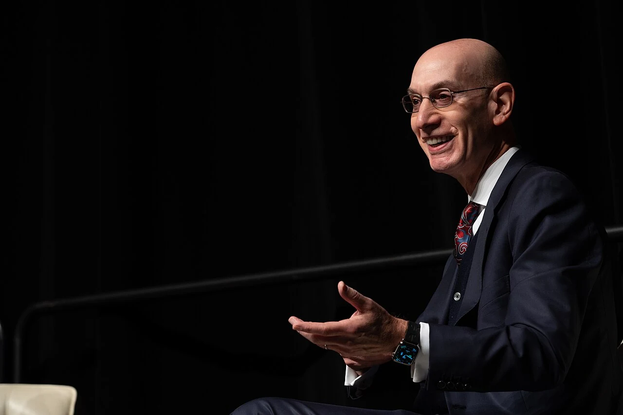 Adam Silver en costume, assis et échangeant lors d’un événement du NBA All-Star Game 2024.