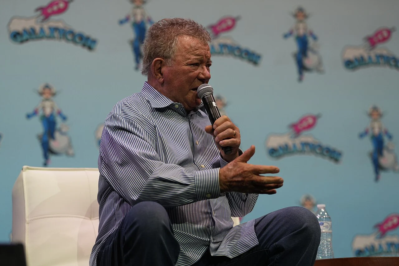 William Shatner assis sur scène, micro à la main, à GalaxyCon Raleigh en 2024.