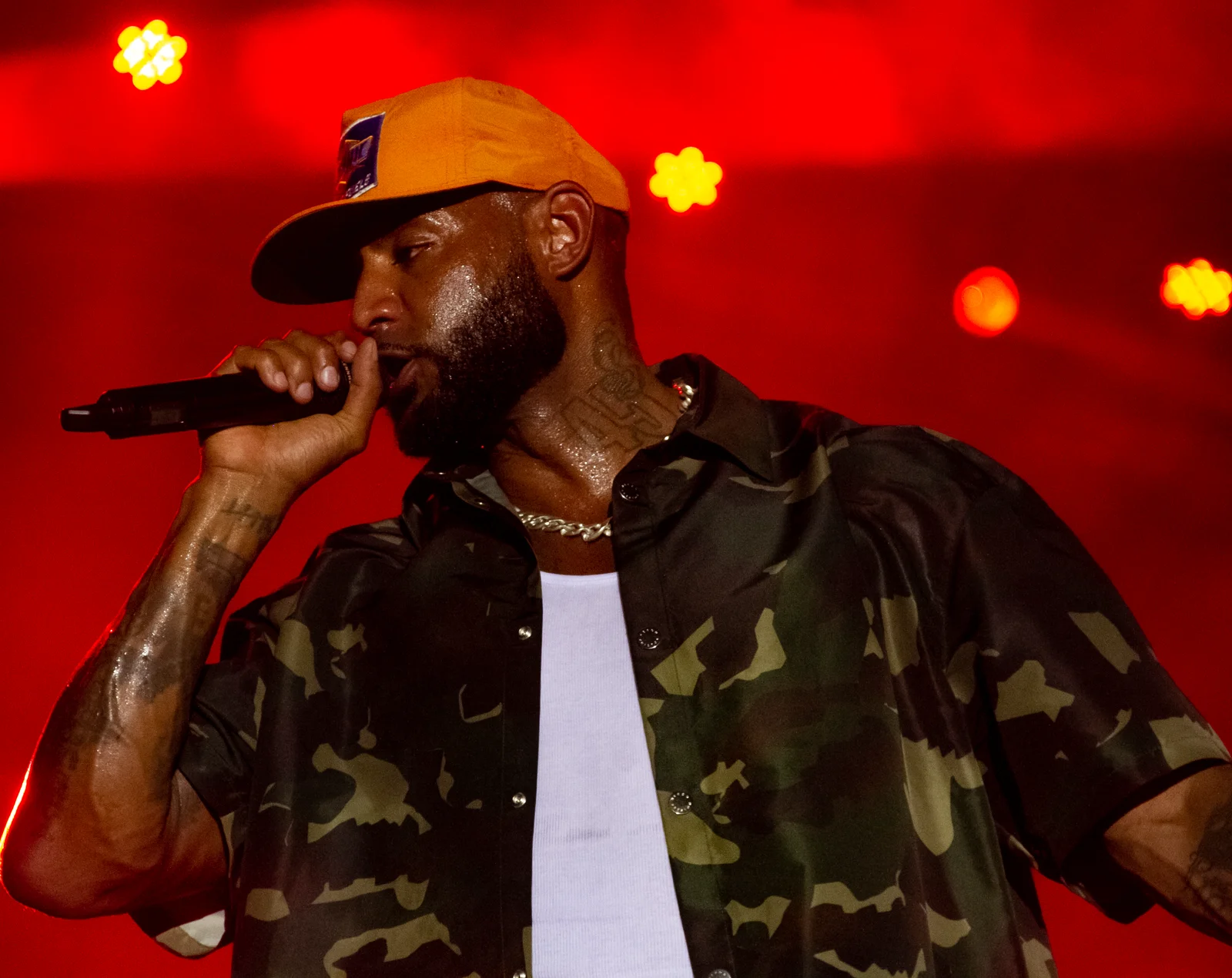 Booba au micro sous une lumière rouge, casquette orange et chemise camouflage, sur la scène du FEMUA à Abidjan.