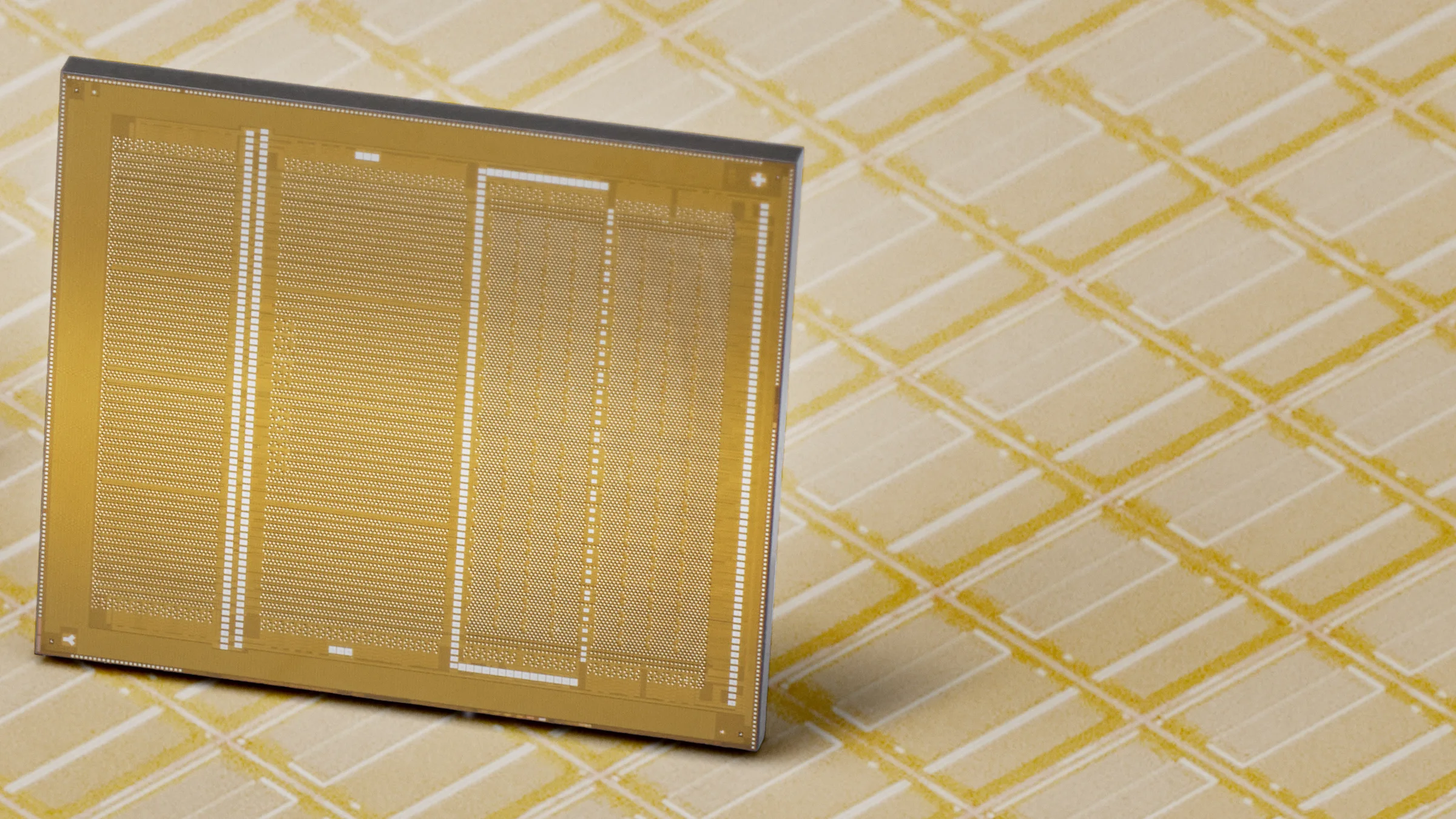 Une puce de mémoire HBM4 de Samsung, vue de dessous, face dorée couverte de contacts, posée debout sur une plaquette de silicium aux motifs dorés.