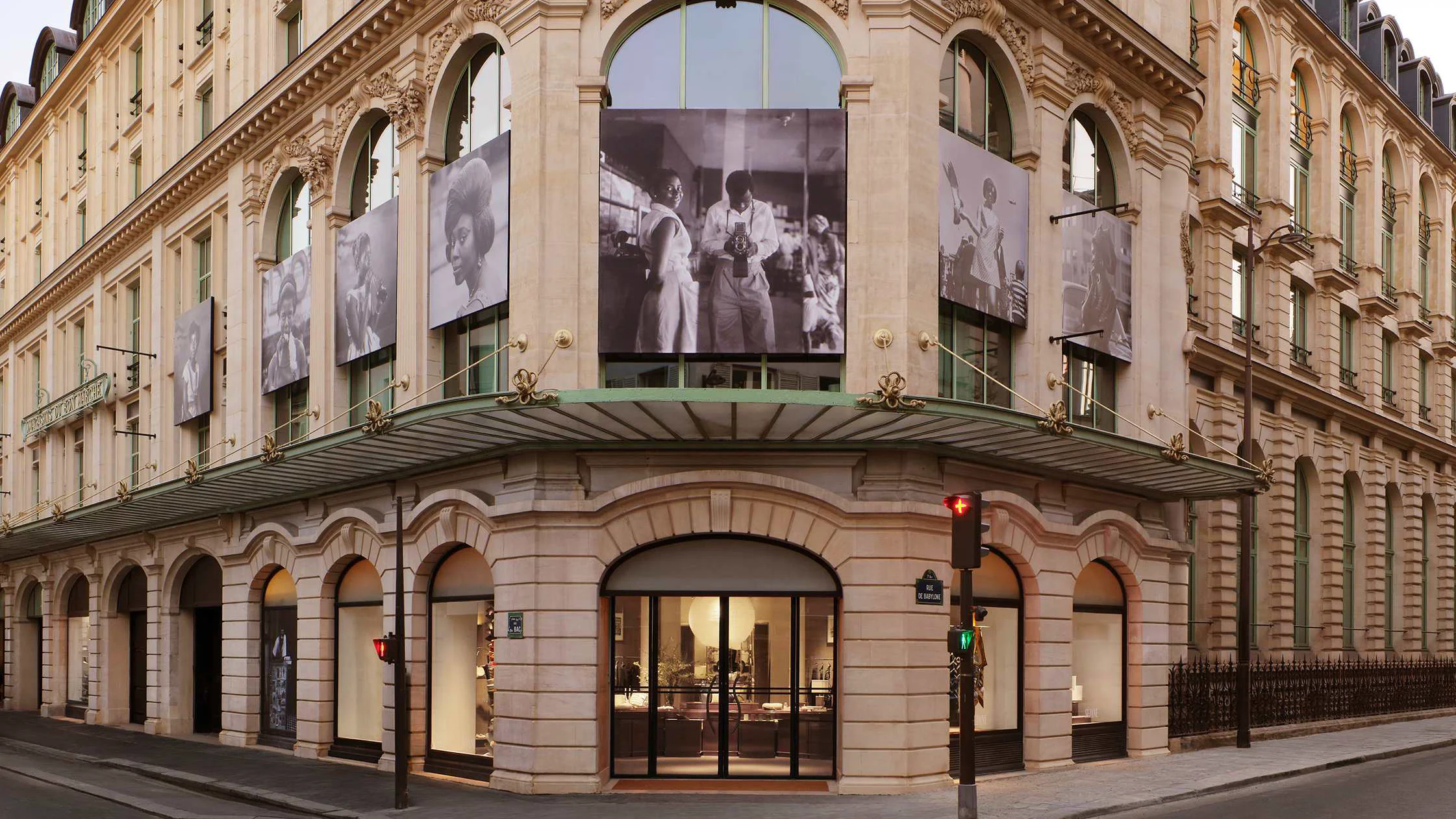 Façade haussmannienne à l’angle de la rue du Bac et de la rue de Babylone, à Paris, avec une marquise verte, une entrée vitrée éclairée et de grands tirages en noir et blanc du photographe James Barnor accrochés aux fenêtres.