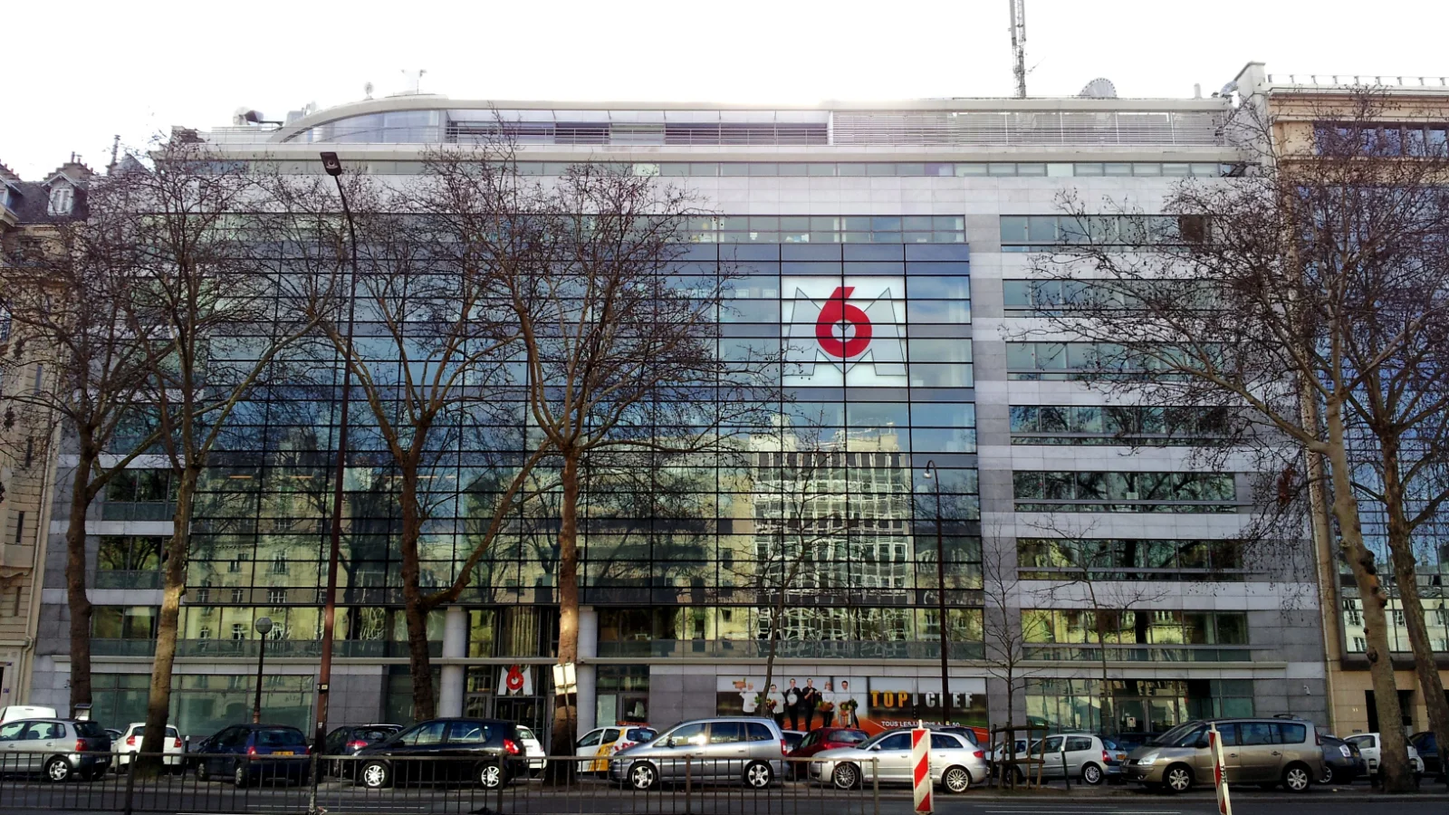 Façade vitrée du siège du groupe M6, avenue Charles-de-Gaulle à Neuilly-sur-Seine, derrière une rangée d'arbres sans feuilles