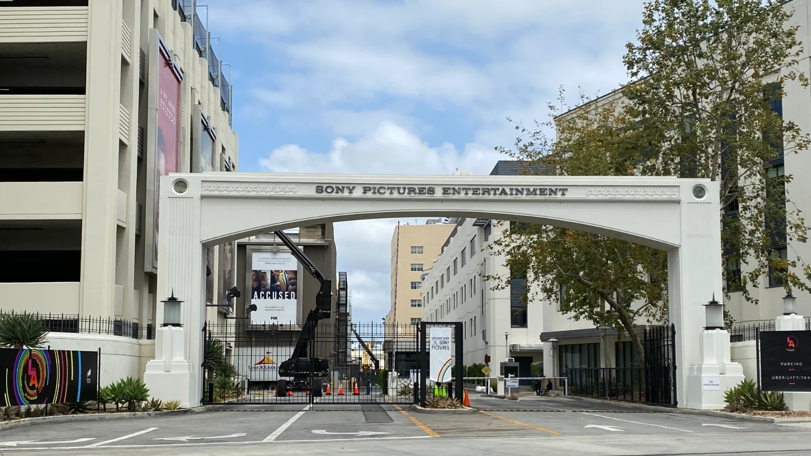 Portail blanc en arche des studios Sony Pictures sur Culver Boulevard, avec une barrière fermée, des bâtiments de bureaux de part et d'autre et un ciel nuageux.