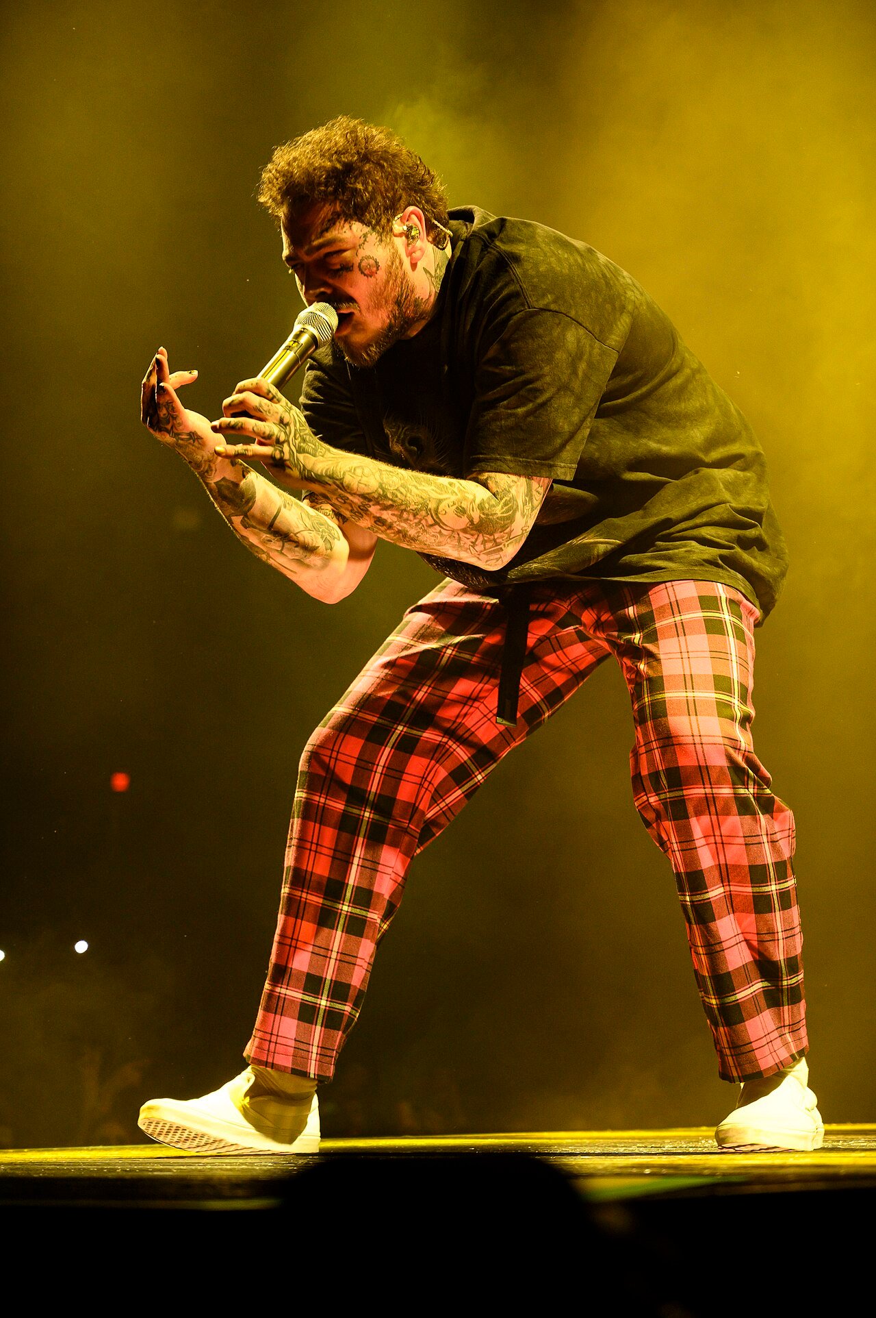 Post Malone chante au micro sur scène sous une lumière jaune lors d’un concert près de Chicago en 2020.
