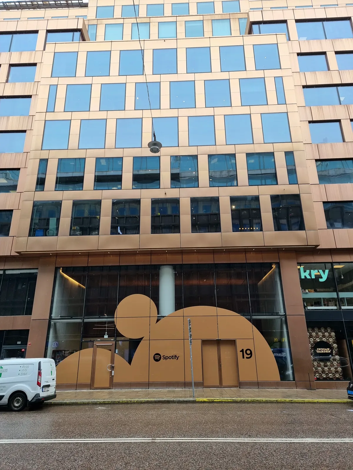 La façade vitrée du siège de Spotify à Stockholm, avec une sculpture en forme de logo au rez-de-chaussée.