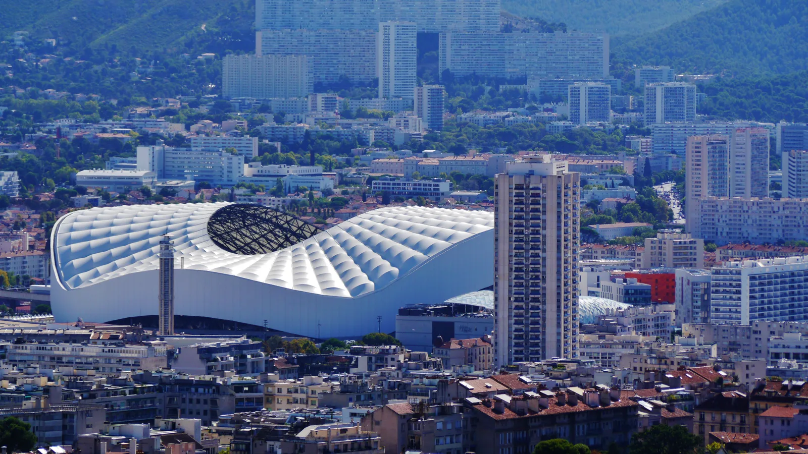 Le stade Vélodrome de Marseille et son toit blanc, vus depuis Notre-Dame-de-la-Garde, devant les collines.