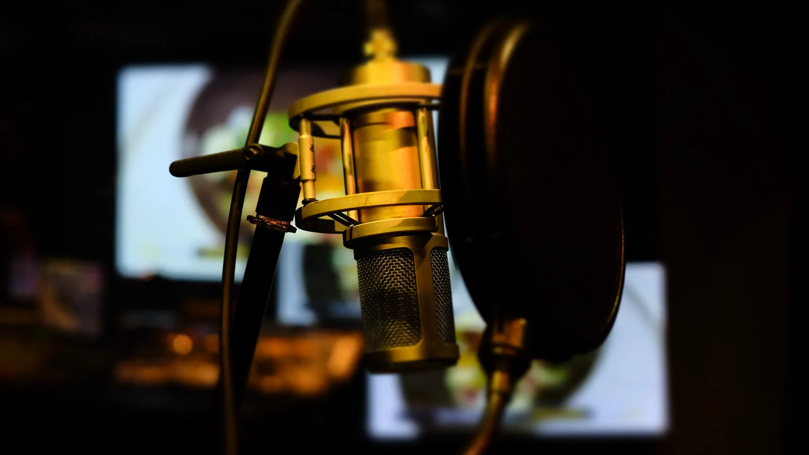 Un micro de studio doré devant des écrans flous qui diffusent des images en cours de montage, dans une salle de mixage plongée dans la pénombre