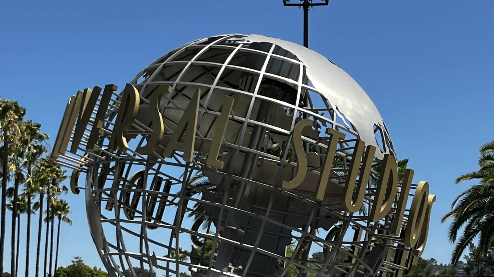 Le globe métallique d’Universal Studios à Hollywood, sous un ciel bleu, entouré de palmiers.