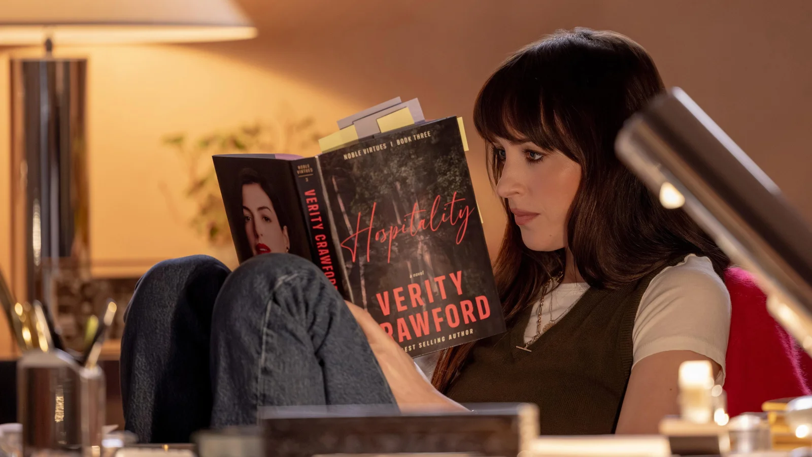 Dakota Johnson, dans le rôle de Lowen Ashleigh, lit un roman de Verity Crawford à la lumière d’une lampe dans Verity.