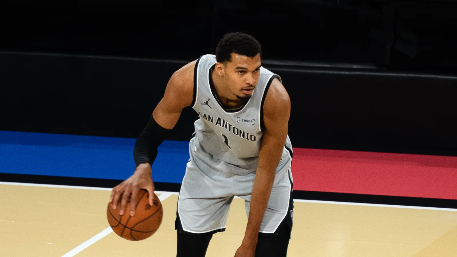 Victor Wembanyama, en maillot gris des San Antonio Spurs, dribble le ballon de la main droite, penché en avant sur le parquet.