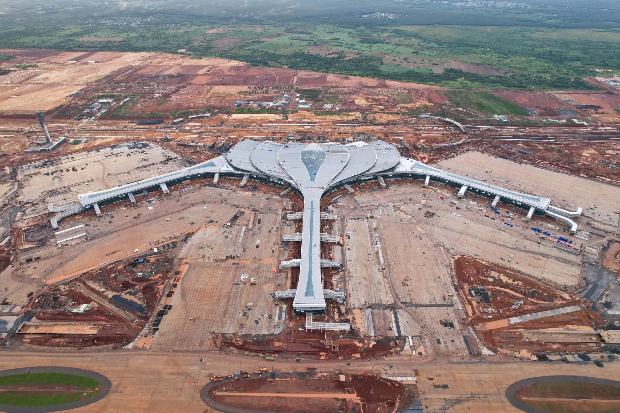 Vue aérienne du terminal de l’aéroport de Long Thành, en forme de fleur de lotus, entouré de pistes et de terrains en chantier.