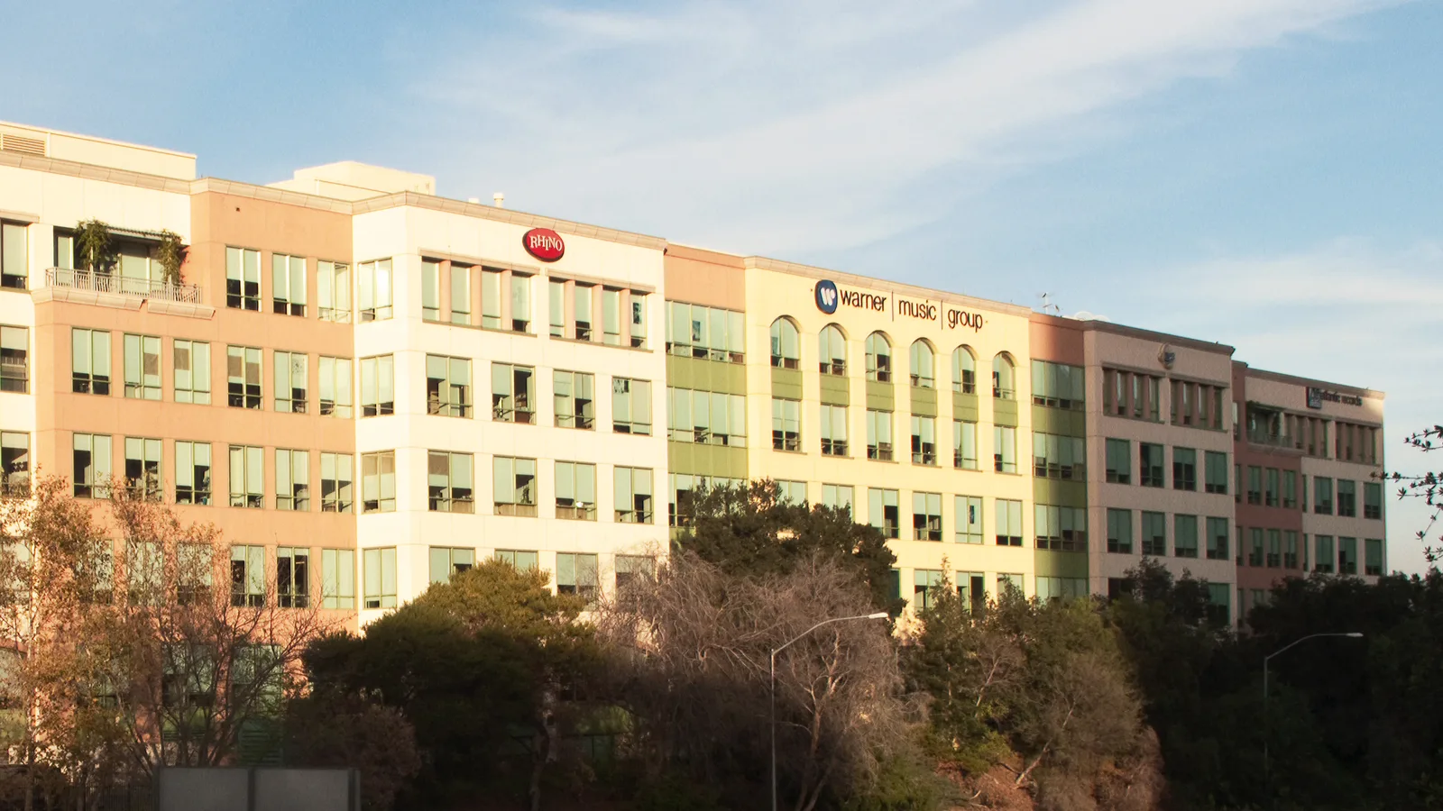 Les bureaux de Warner Music Group à Burbank, en Californie : une longue façade claire avec le logo du groupe, au soleil couchant.