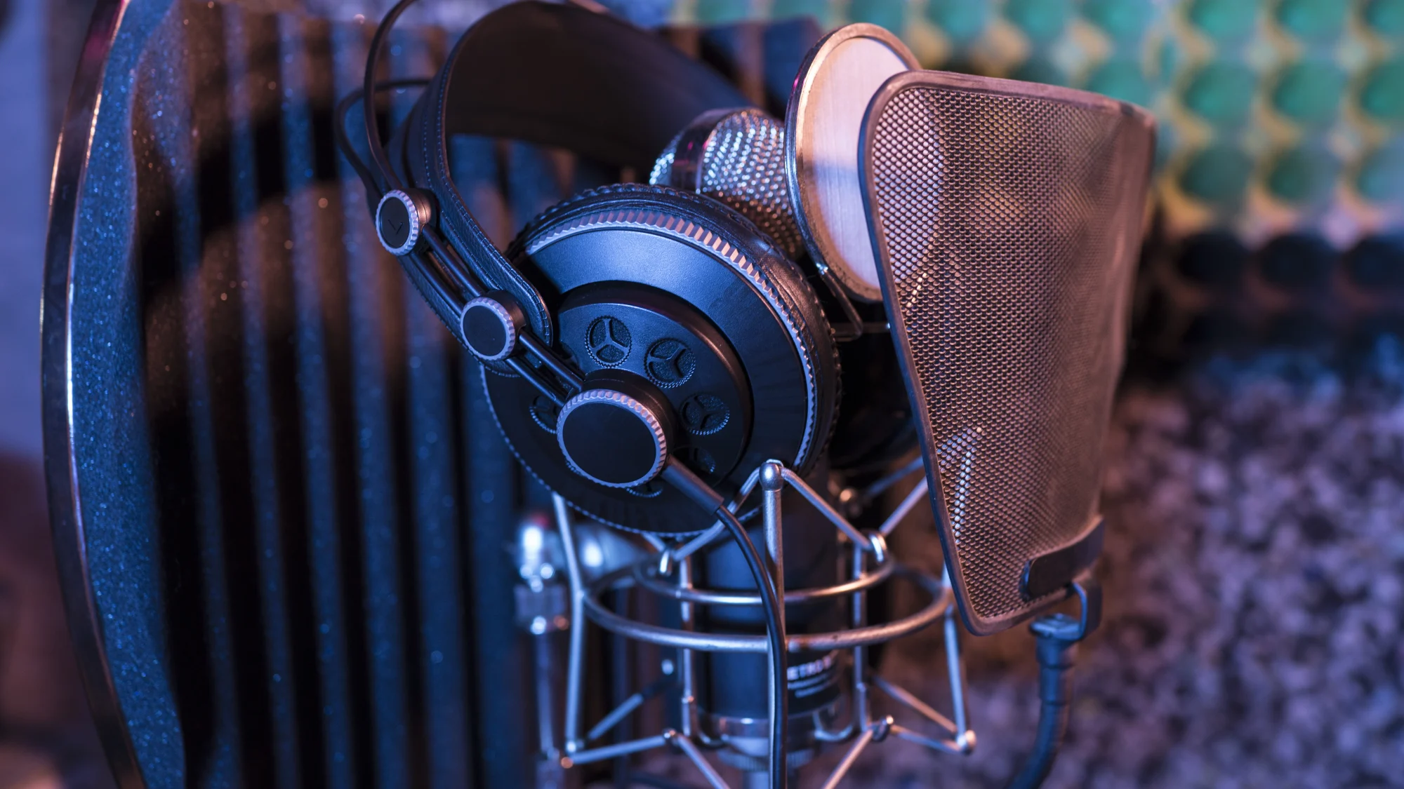 Un casque de studio posé sur un micro à condensateur équipé d’un filtre anti-pop, dans une cabine d’enregistrement éclairée de bleu et de violet.