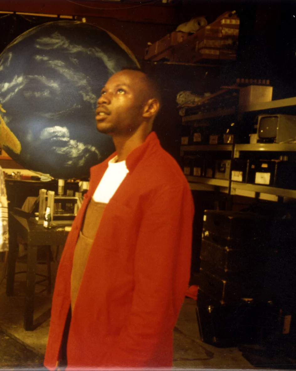 MC Solaar, chemise rouge sur tee-shirt blanc, lève les yeux devant un grand globe terrestre, au studio Excalibur de Joinville, en août 1994.