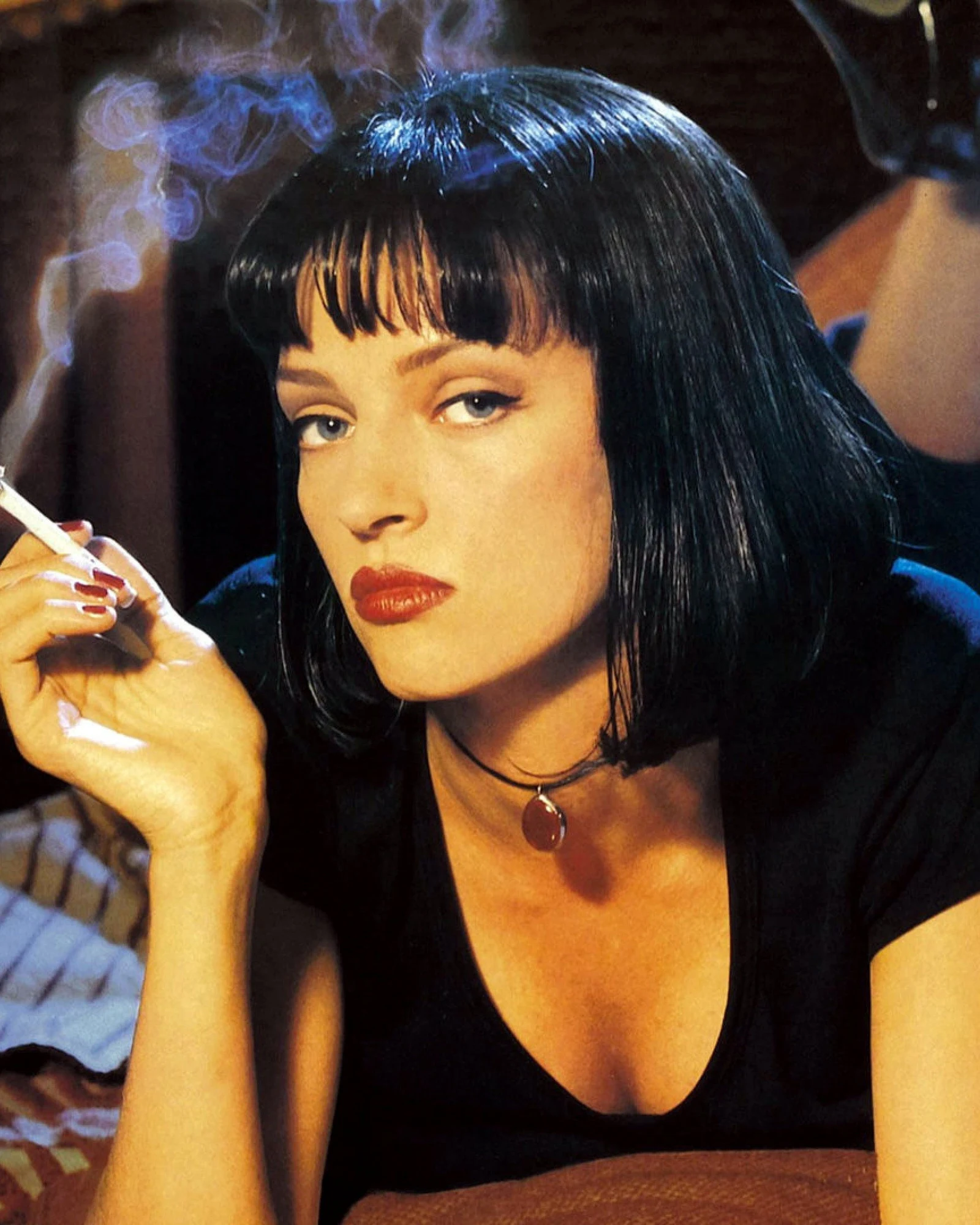 Uma Thurman en Mia Wallace, carré noir, rouge à lèvres rouge et cigarette à la main, allongée sur un lit, sur la photo promotionnelle de Pulp Fiction.