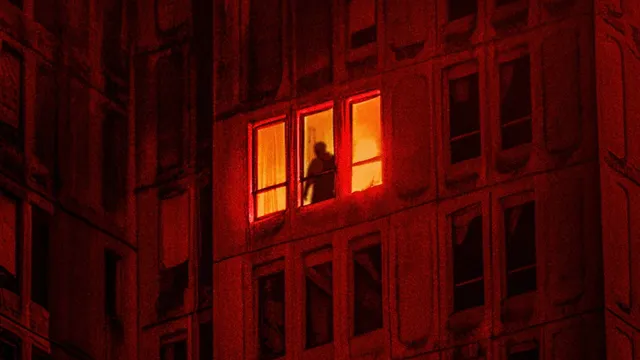 Image officielle de Kraken : une silhouette derrière une fenêtre éclairée, dans un immeuble baigné de rouge.